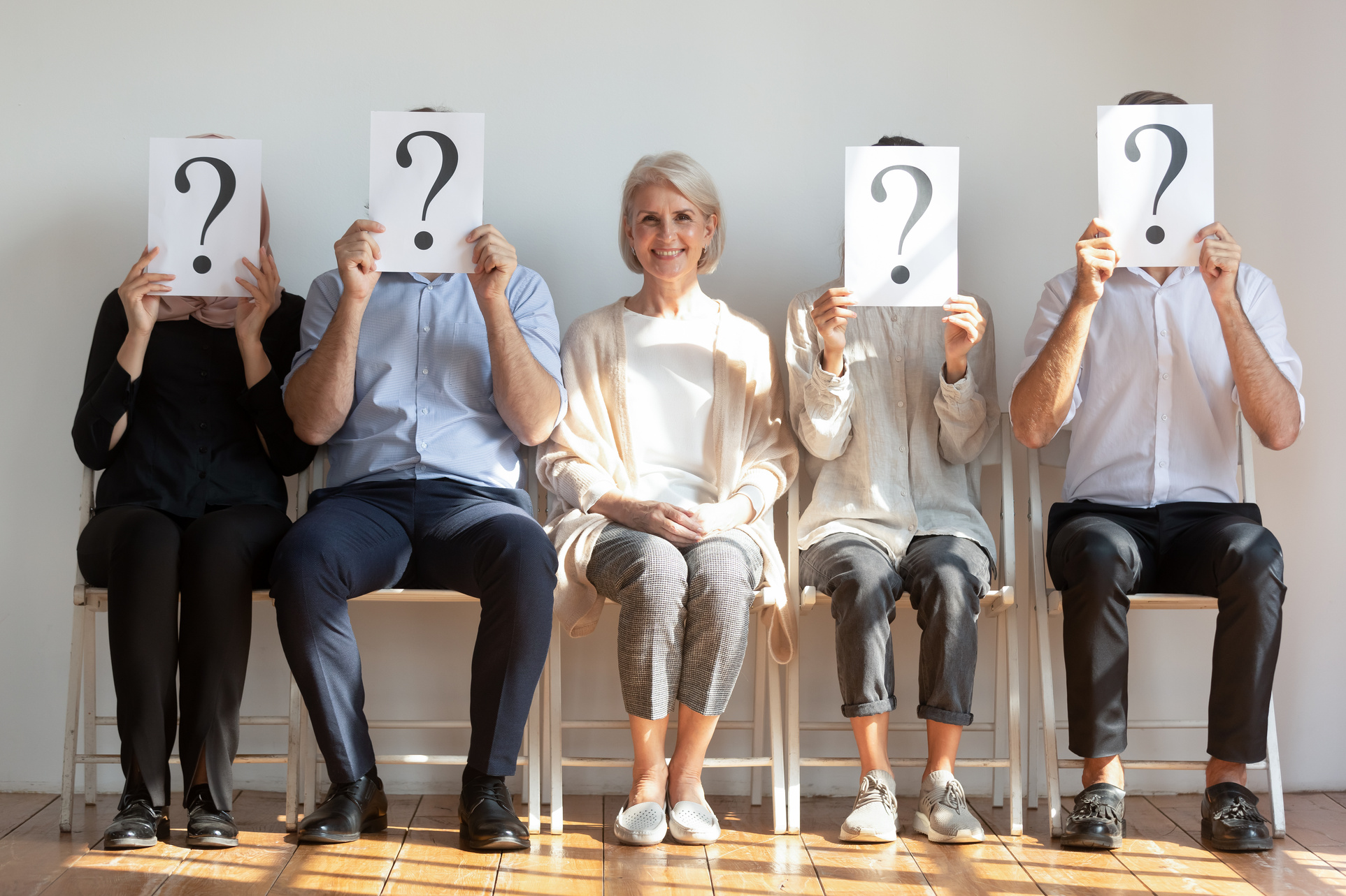 Mature Businesswoman Sitting among People Holding Boards with Question Marks